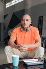 Bald man in coffee shop wearing headphones and orange polo shirt while praying