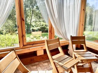 Showcases minimalist wooden chairs in a bright, airy cabin surrounded by nature. 