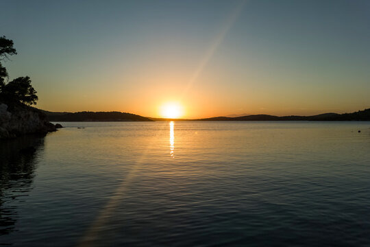 Idyllic Sunset Over Serene Sea with Rocky Coastline and Pine Trees. Tranquil Nature Landscape, Golden Hour, Calm Water, Peaceful Scenery, Travel Destination, Coastal View, Summer Evening Vibes