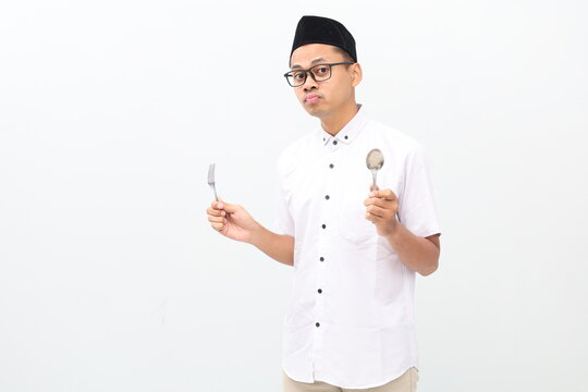 Sad confused asian muslim man holding spoon and frok with unhappy face expression