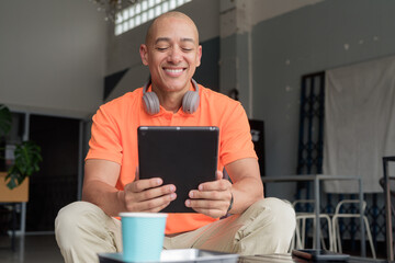Smiling bald Hispanic man using digital tablet computer in coffee shop