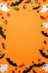 Halloween Flat Lay with Colorful Candies, Bat and Ghost Cutouts on Orange Background with Copy Space
