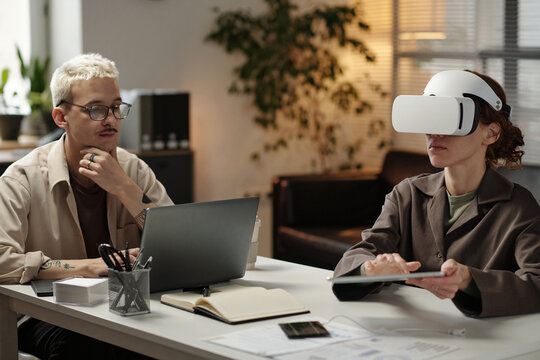 Young gen Z female manager using digital tablet and VR headset while her male colleague looking at laptop screen in modern office