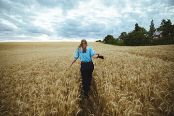 A woman walking in a wheat field holding a camera.