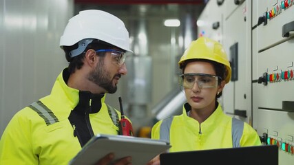 Technicians using digital tablets to discuss cooling system upgrades and electricity usage in an industrial control cabinet.
