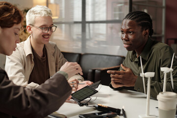 Group of three young ethnically diverse engineers sitting at office desk, discussing renewable energy solutions