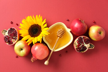 Rosh Hashanah still life with honey, apples, pomegranates, and sunflower on red background....