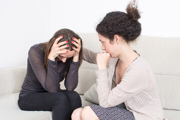 A young woman consoles her sad friend on the sofa, offering emotional support and compassion. Concept of friendship, empathy, care, and counseling in difficult times.