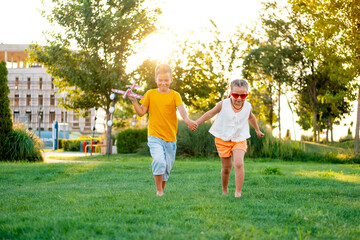 Obraz premium little children flying a plane, a boy and a girl playing with a plane on a green lawn, laughing children on the grass in summer, summer holidays