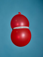 Red balloon with a measuring tape against a blue background as a symbol of eating less or reducing the stomach size