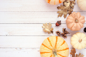 Autumn side border of pumpkins, golden leaves and natural decor. Overhead view on a white wood background with copy space.