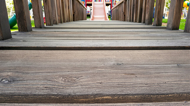 Low Angle Perspective of Weathered Wooden Walkway Leading to a Colorful Outdoor Children's Playground with Red Slide and Green Grass