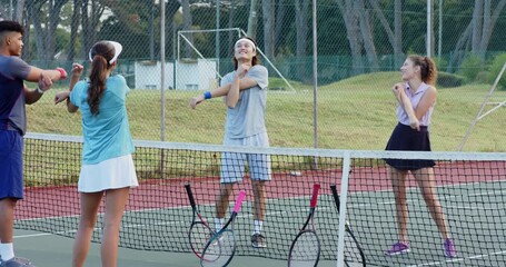Second man joining diverse friends warming up with arm stretches on tennis court, tossing ball