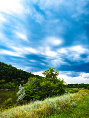 The blue sky above the forest is reflected in the lake along which a dirt road runs.