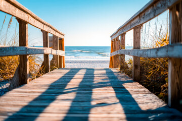 Wooden boardwalk leading to a sandy beach and ocean under clear blue sky