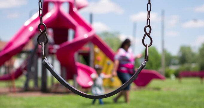 Empty Swing in park with mother and daughter walking by 4k
