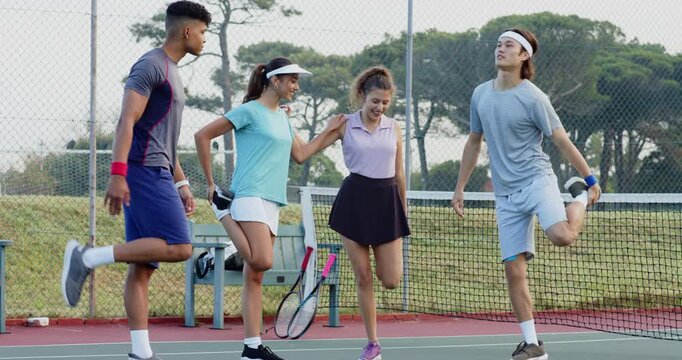 Dropping rackets on bench at net, Diverse tennis pals alternating leg stretches preparing for play