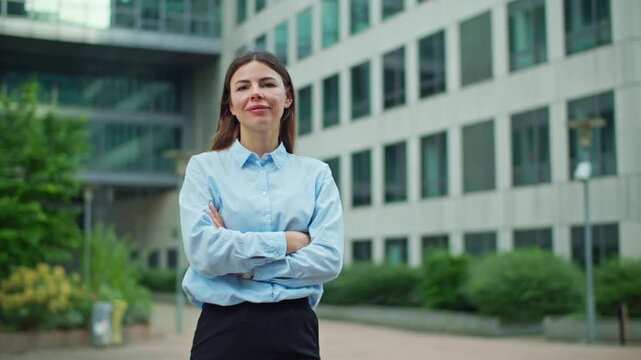 Young elegant female professional employee standing in front of a high rise office tower confidently smiling in a modern financial area showing urban corporate identity