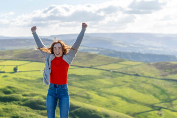 Joyful young woman celebrates on a rocky outcrop in the hills while clouds drift across a bright blue sky in the afternoon light