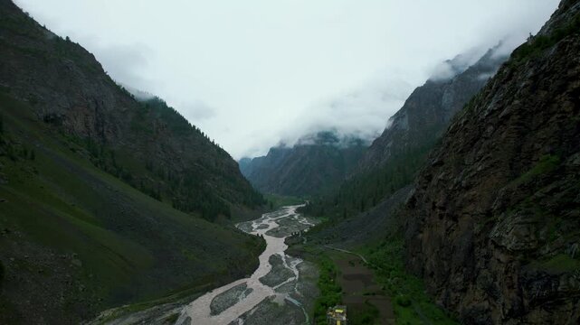 4K Aerial shot of Miyar river flowing among mountains background. Idyllic green scenery and monsoon clouds on peaks. Nature backgrounds. 
