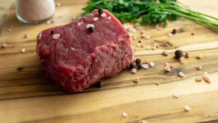 close up of a piece of fresh beef on a wooden cutting board. farm fresh meat with coarse salt and herbs on the table