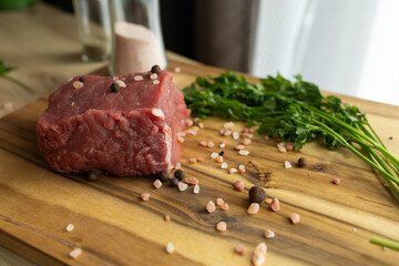 close up of a piece of fresh beef on a wooden cutting board. farm fresh meat with coarse salt and herbs on the table
