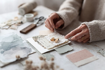 Closeup of hands assembling a delicate craft project. Artsy, layered papers, butterfly embellishment. Evokes creativity, scrapbooking, journaling, handmade design.