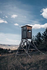 Wooden hunting lookout tower standing in a meadow with scenic countryside view and blue sky background.