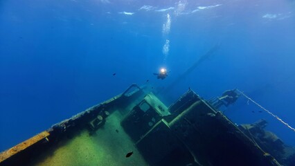 Shallow sea with scuba diver explore on the rusty metal shipwreck. Scuba diver and part of the wreck. Scuba diving trip, wreck exploration. Travel photo, shipwreck and photographing diver.