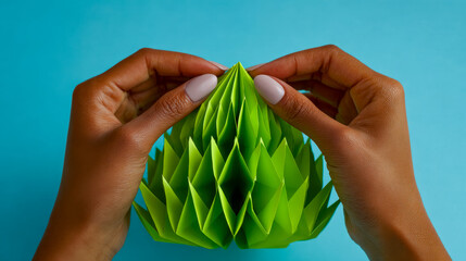 Hands adjusting a vibrant green paper origami sculpture against a blue background