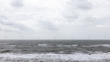 Offshore wind farm on stormy sea with waves under dramatic cloudy sky 
