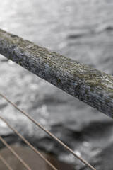 Wooden railing with lichen above steel cables, water and stone on riverside bridge
