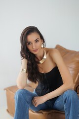 Obraz premium Beautiful tall thin brunette with curly hair in living room. The girl in black korset and jeans, room background. Studio photo shoot for a model. Portrait.