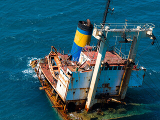 Partially submerged Manassa Rose shipwreck with rusted structure, yellow and blue funnel, and...