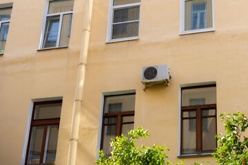 Fototapeta premium air conditioner on wall of an apartment building with view of green trees. ventilation and cooling of home or office during hot weather. installation maintenance of fan air conditioner. summer heat