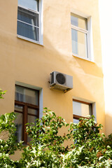 air conditioner on wall of an apartment building with view of green trees. ventilation and cooling of home or office during hot weather. installation maintenance of fan air conditioner. summer heat