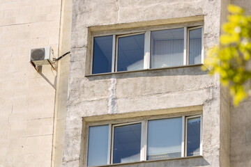 air conditioner on wall of an apartment building with view of green trees. ventilation and cooling of home or office during hot weather. installation maintenance of fan air conditioner. summer heat