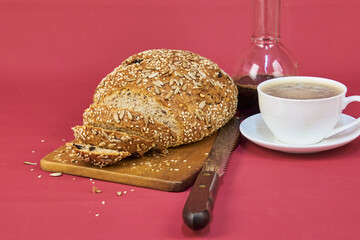 Homemade bread on a wooden board next to a cup of coffee in the foreground with a cherry-colored background