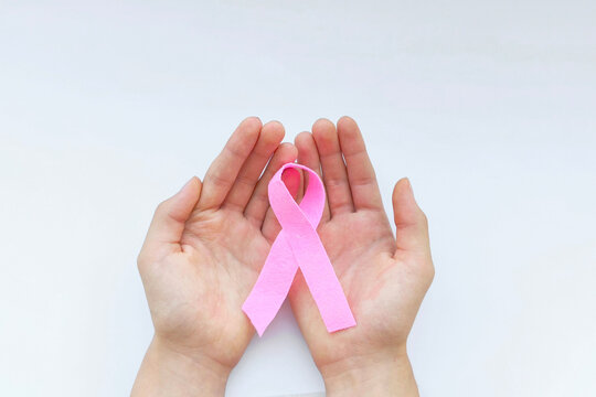Close up of hands holding pink ribbon on white background with copy space. Breast Cancer Awareness Month. Support and promotion of campaign against cancer. Healthcare concept. Pink October - Powered by Adobe