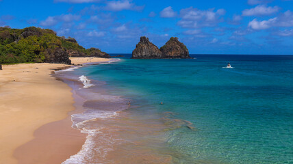 Fototapeta premium Vista aérea da Praia do Boldró, Noronha, com falésias, vegetação tropical, águas cristalinas e os Dois Irmãos ao fundo, cenário perfeito de férias na ilha