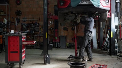 An auto mechanic is performing a routine engine oil change in a service station. A professional worker uses a special wrench to loosen the old oil filter before replacing it with a new one.