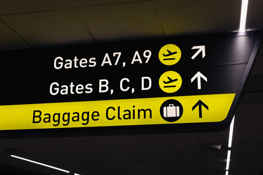 Airport directional sign with yellow and black background. Information board showing gates and baggage claim area. Modern terminal signage with arrows and icons. Travel and transportation guidance.