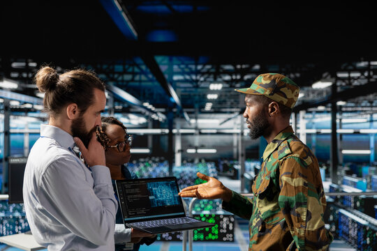 Army technicians in command center server farm using artificial intelligence to detect cyber threats. Military data center IT experts use AI detection software to secure defense systems.