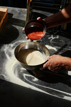 Vertical high angle view shot of unrecognizable chef adding red mixture to flour in stainless steel bowl