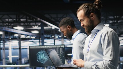 Technician holding laptop walking on server farm platform, doing AI machine learning automatization. Data center programmer using notebook, doing maintenance using artificial intelligence