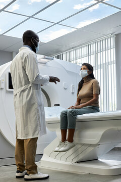 Vertical low angle full length shot of African American doctor standing in front female patient telling her about MRI scanning process