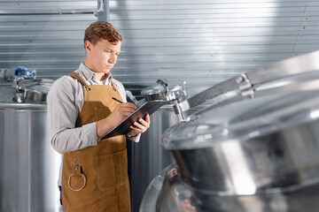 Young caucasian male brewer assessing brewery equipment levels during inspection. Concept food industry with quality craft beer product