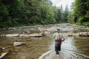 Fisherman wading in river fishing for trout in pristine nature