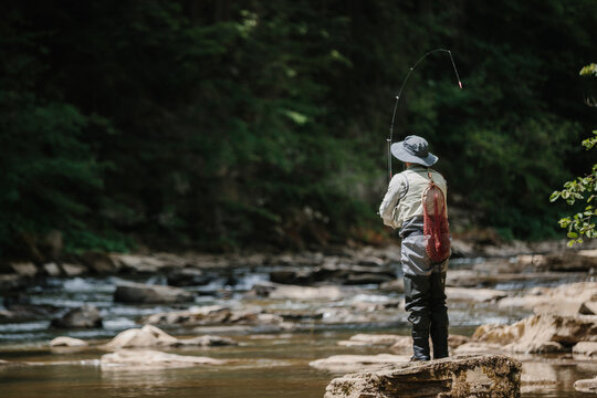 Fisherman casting line in river, catching trout on sunny day