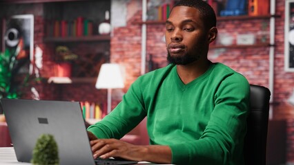 African american teleworker experiences lower back pain due to incorrect posture sitting at desk, dealing with office syndrome and muscle cramps. Young man feels overworked. Camera B.